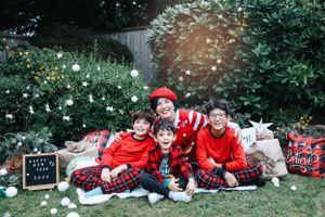 Family group in matching red outfits pose on a blanket with Christmas decorations and falling snow effect.