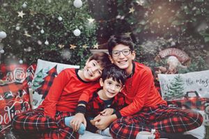 Holiday portrait with matching red tops and plaid pajamas against Christmas-themed backdrop.