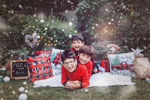 Festive holiday photo with people in red outfits lying on white blanket surrounded by Christmas decorations.