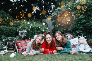 Three people in festive attire pose on blanket with holiday decorations and twinkling lights.