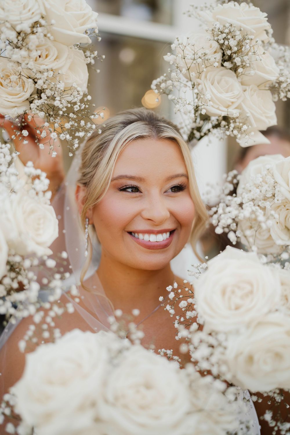 Beautiful white roses and baby's breath flowers frame a joyful bridal portrait at an elegant wedding celebration.