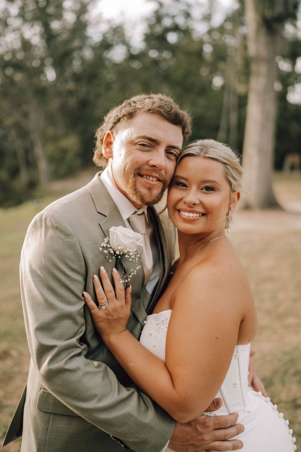 A happy couple embraces outdoors on their wedding day wearing a tan suit and white strapless dress.