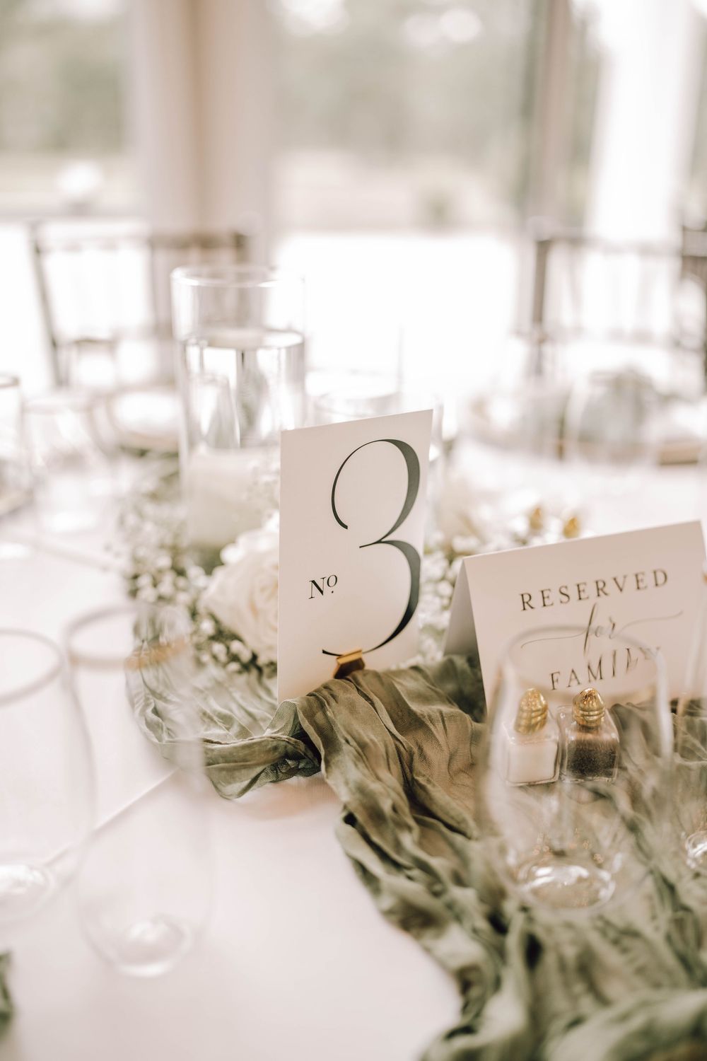 Wedding reception table settings with reserved cards and greenery decorations in soft focus.
