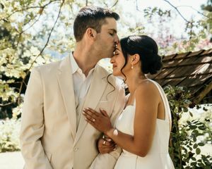 Romantic moment captured under blooming spring trees at outdoor wedding venue.