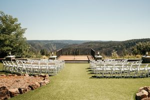 A panoramic view of a rustic outdoor wedding ceremony setup with white chairs and mountain scenery in the background.