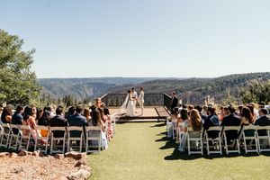 Outdoor wedding ceremony overlooking a scenic mountain landscape with guests seated on white chairs.