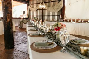 Elegant wedding reception table settings with rustic decor, white linens, and crystal glassware in a barn venue.