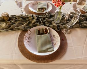 Close-up of rustic wedding table decor featuring twisted garland, white plates, and brown charger placemats.