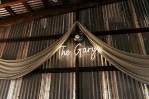 Rustic wedding venue with illuminated 'The Garys' neon sign and draped fabric decor.