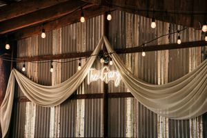 White fabric draping and string lights create an elegant ceiling decoration in a rustic venue.