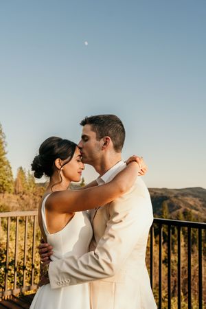 A couple shares an intimate moment at sunset on a balcony overlooking mountain scenery.