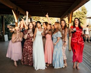Wedding party guests in coordinated dresses dancing together under a covered outdoor venue with string lights.