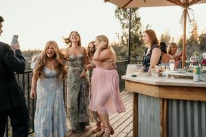 Wedding guests in pastel dresses mingle and celebrate during an outdoor reception.