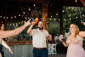 Group of wedding guests dancing and raising their drinks during a celebration under string lights.