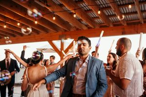 Wedding reception guests dancing and celebrating under rustic wooden beams with string lights.