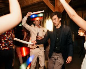 People dancing and celebrating at a lively wedding reception with colorful lights and drinks.
