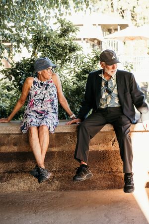 Couple sitting together on a stone wall in a garden setting during a photo session.
