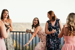 Bridesmaids in navy and pink dresses share joyful laughter on an outdoor balcony during a wedding celebration.
