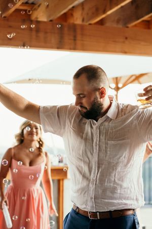 Wedding party celebrates with soap bubbles floating through the air in a rustic wooden venue.