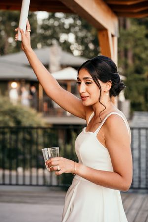 Woman in white dress dancing joyfully at a wedding reception under wooden beams.