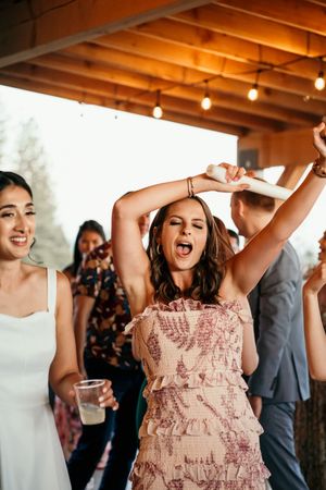 Wedding party guests dancing and celebrating under rustic wooden beams with string lights.