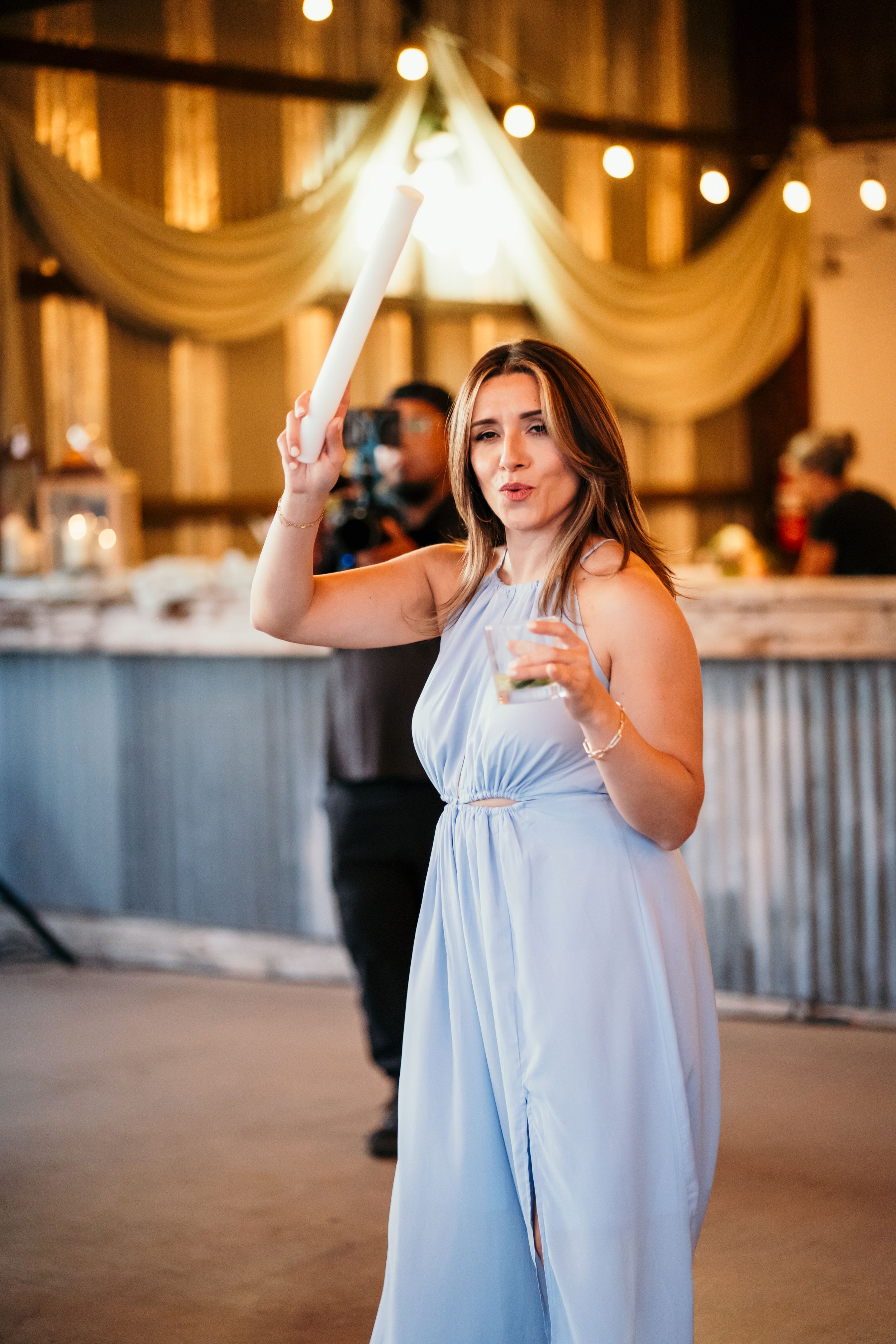 Person in a light blue dress dances energetically at an indoor reception venue with string lights.