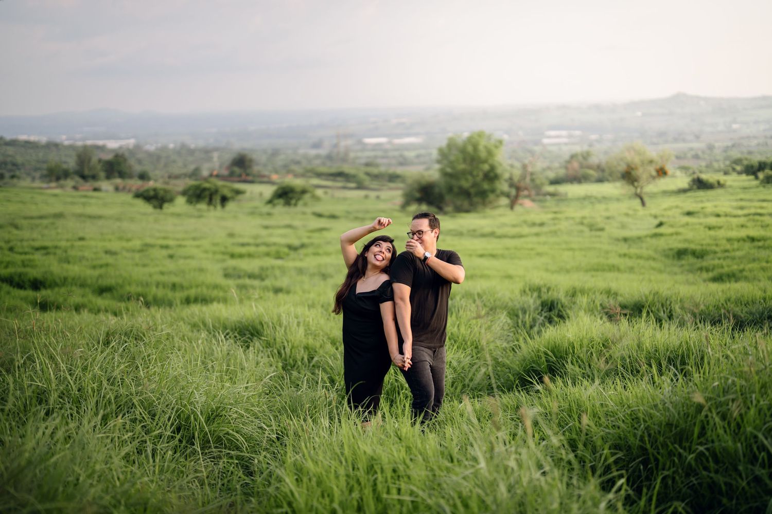 A romantic outdoor photoshoot in a lush green meadow with rolling hills in the background.