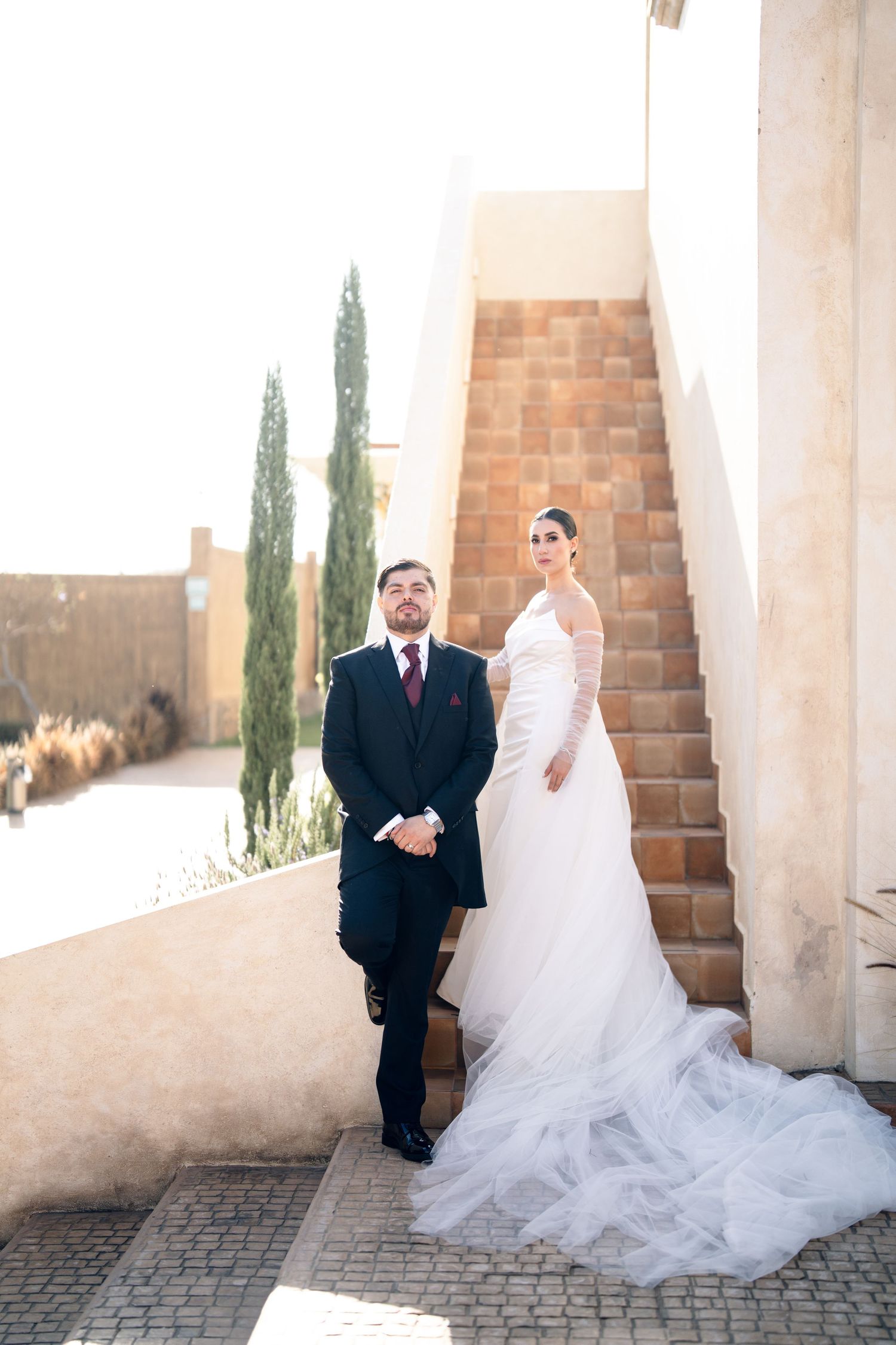Wedding photography session with flowing white dress against architectural columns and cypress trees.