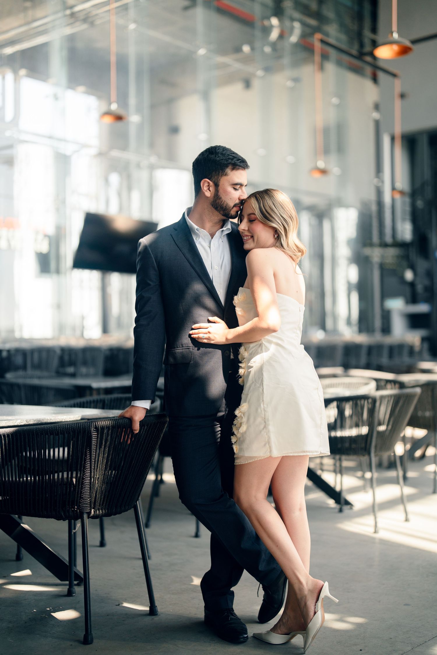 Romantic engagement session in modern industrial space with dramatic window lighting.