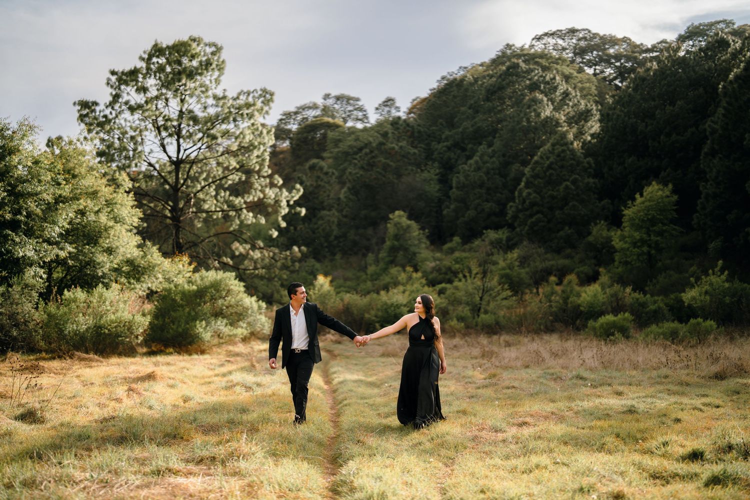 Couple walking through golden field during sunset photoshoot.