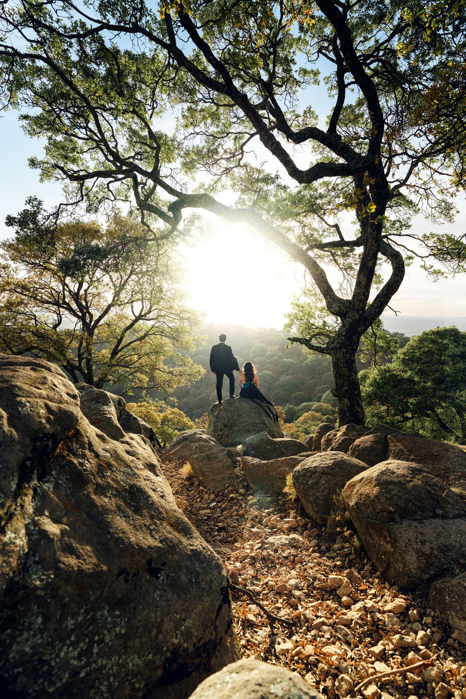Silhouetted figures on rocky outcrop with sunlit trees and autumn leaves.