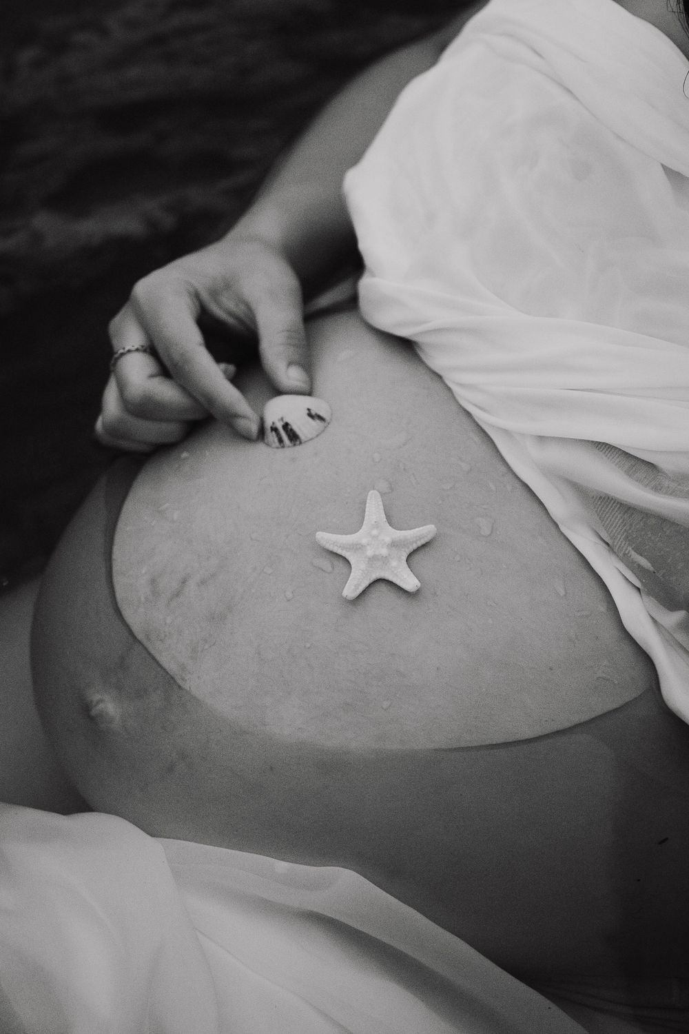 A series of black and white photos showing a starfish being placed on a pregnant belly in an artistic maternity shoot.