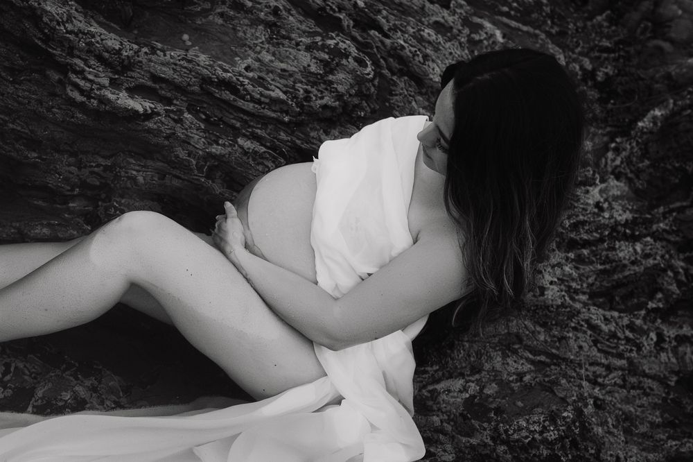 A series of black and white artistic boudoir photos showing a person in white lingerie posing against dark rocks.