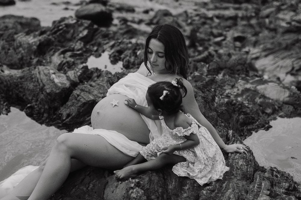 A black and white sequence of photos showing a person playing in shallow water at a rocky beach.