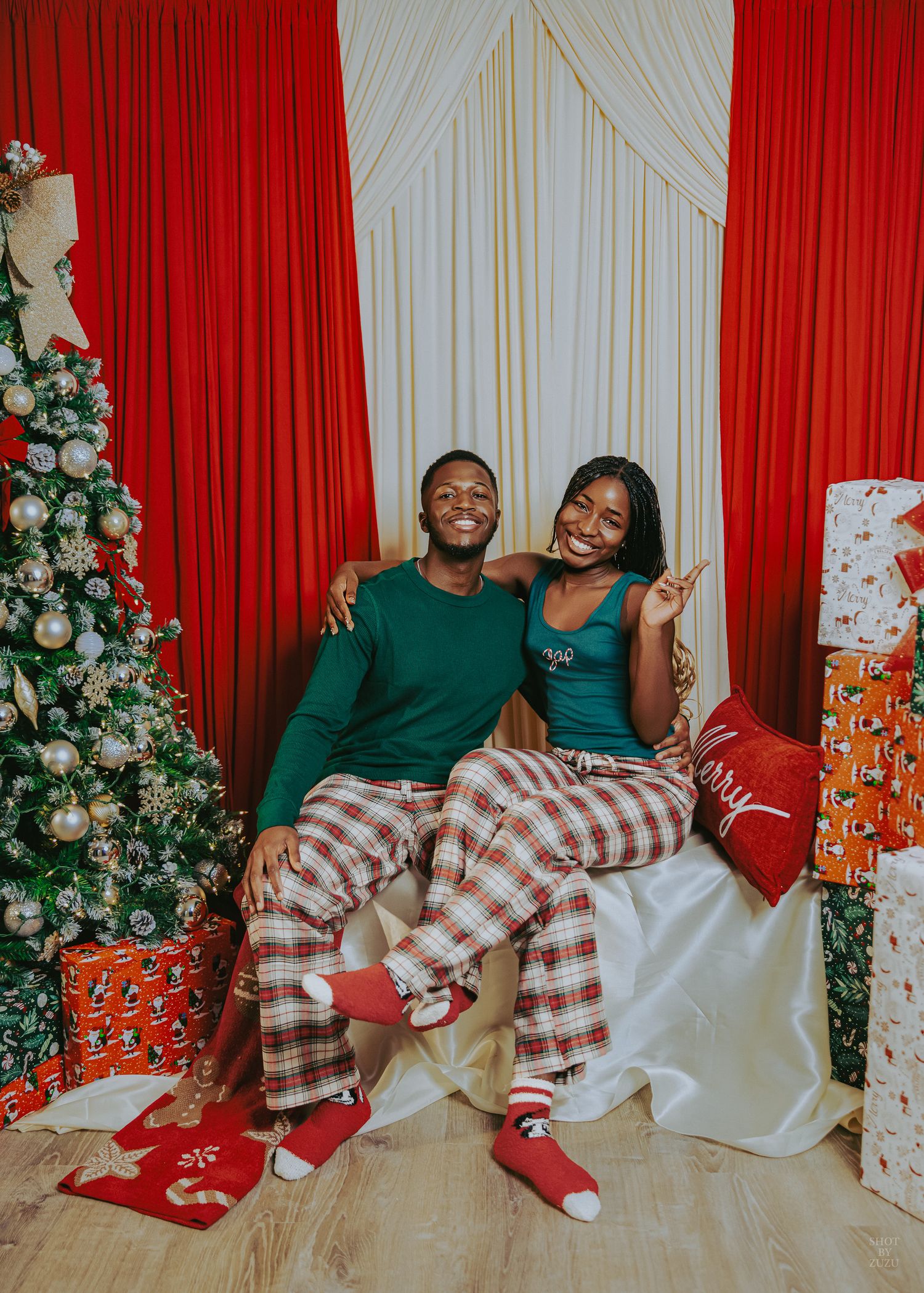 Elegant Christmas scene with decorated tree, silver ornaments, red curtains, and wrapped presents on cream fabric.