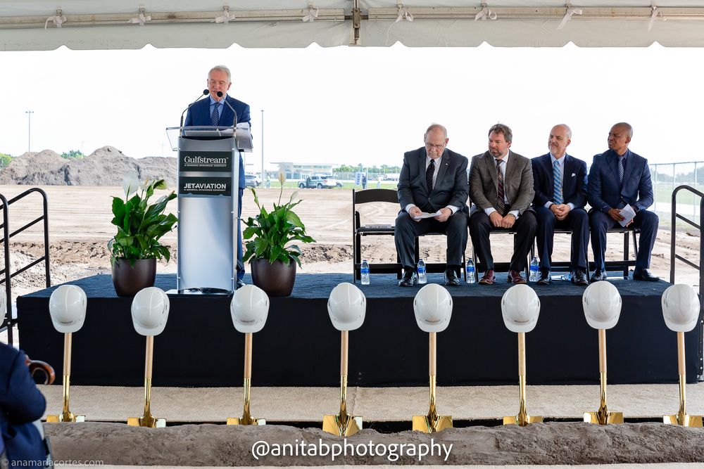 Row of executives in dark suits seated at groundbreaking ceremony with white balloons and shovels.
Ground braking event.