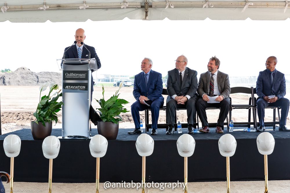 Business leaders lined up on stage with ceremonial shovels and white balloons at corporate event.
Ground braking event.