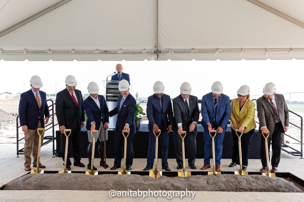 Wide shot of corporate groundbreaking ceremony with executives holding ceremonial shovels.
Ground braking event.