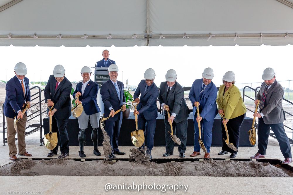 Corporate executives perform ceremonial dirt toss with golden shovels at groundbreaking event.
Ground braking event.