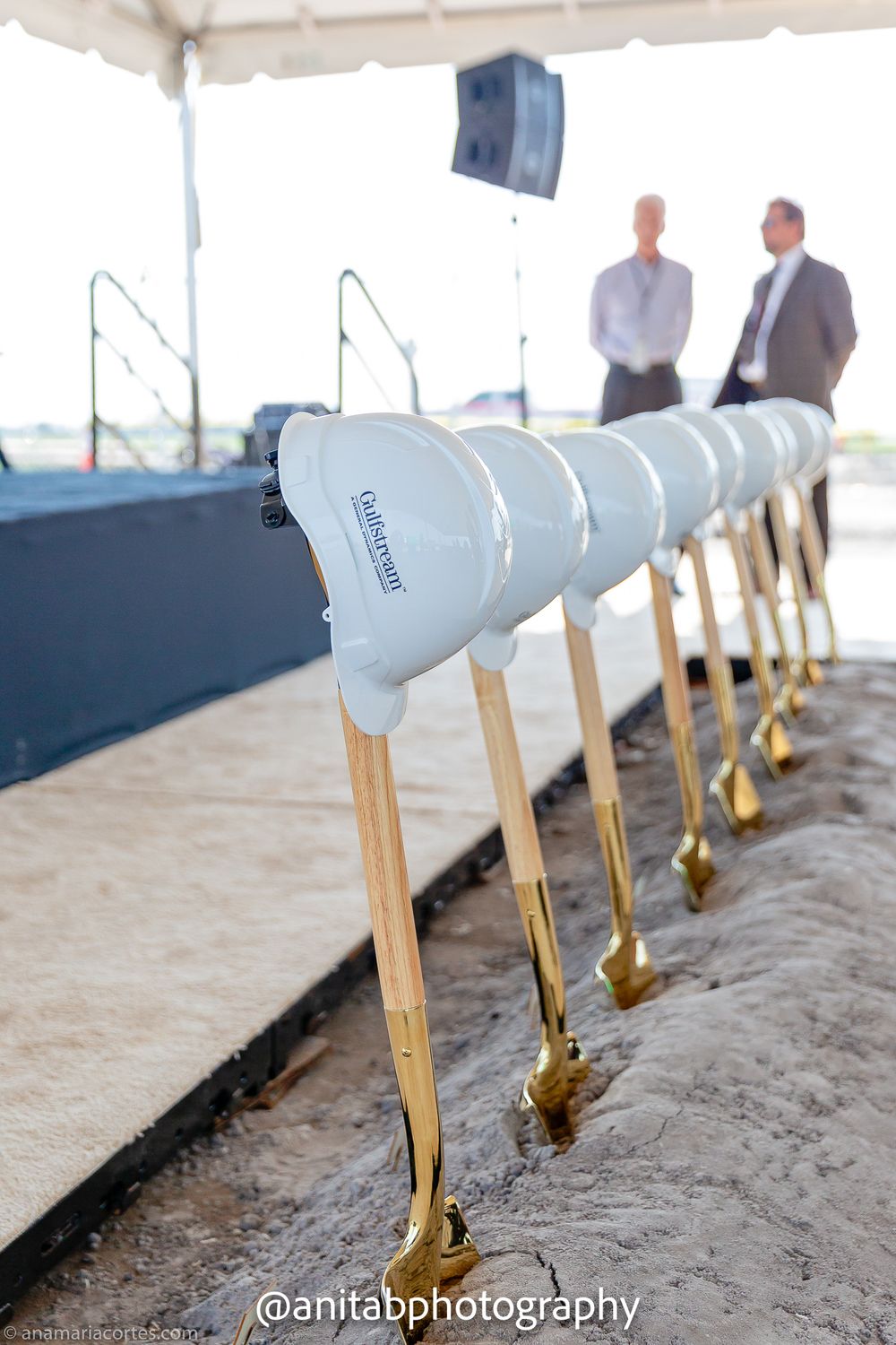 Row of ceremonial groundbreaking shovels with gold handles displayed under a white tent.
Ground braking event.