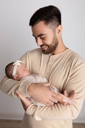 Parent in beige henley shirt holds sleeping newborn wrapped in light-colored swaddle. NJ newborn photographer in Sussex County