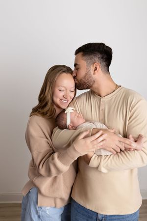 A couple in matching beige sweaters share tender moments in a series of intimate poses against a light background. NJ newborn photographer