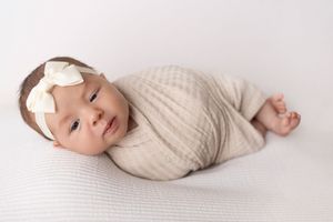 A sleeping baby wearing a cream colored knit sweater lies peacefully on white bedding. NJ newborn photographer in Sussex County