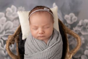Newborn baby sleeping peacefully in a grey knit wrap against a soft grey background. Best newborn photographer in Sussex County NJ