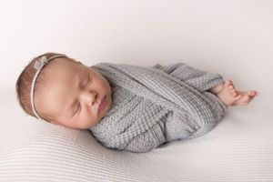 Sleeping infant wearing gray knit sweater rests peacefully on white bedding in natural light.