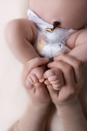 Close-up of baby's tiny feet and toes while wearing white diaper with gold accents.