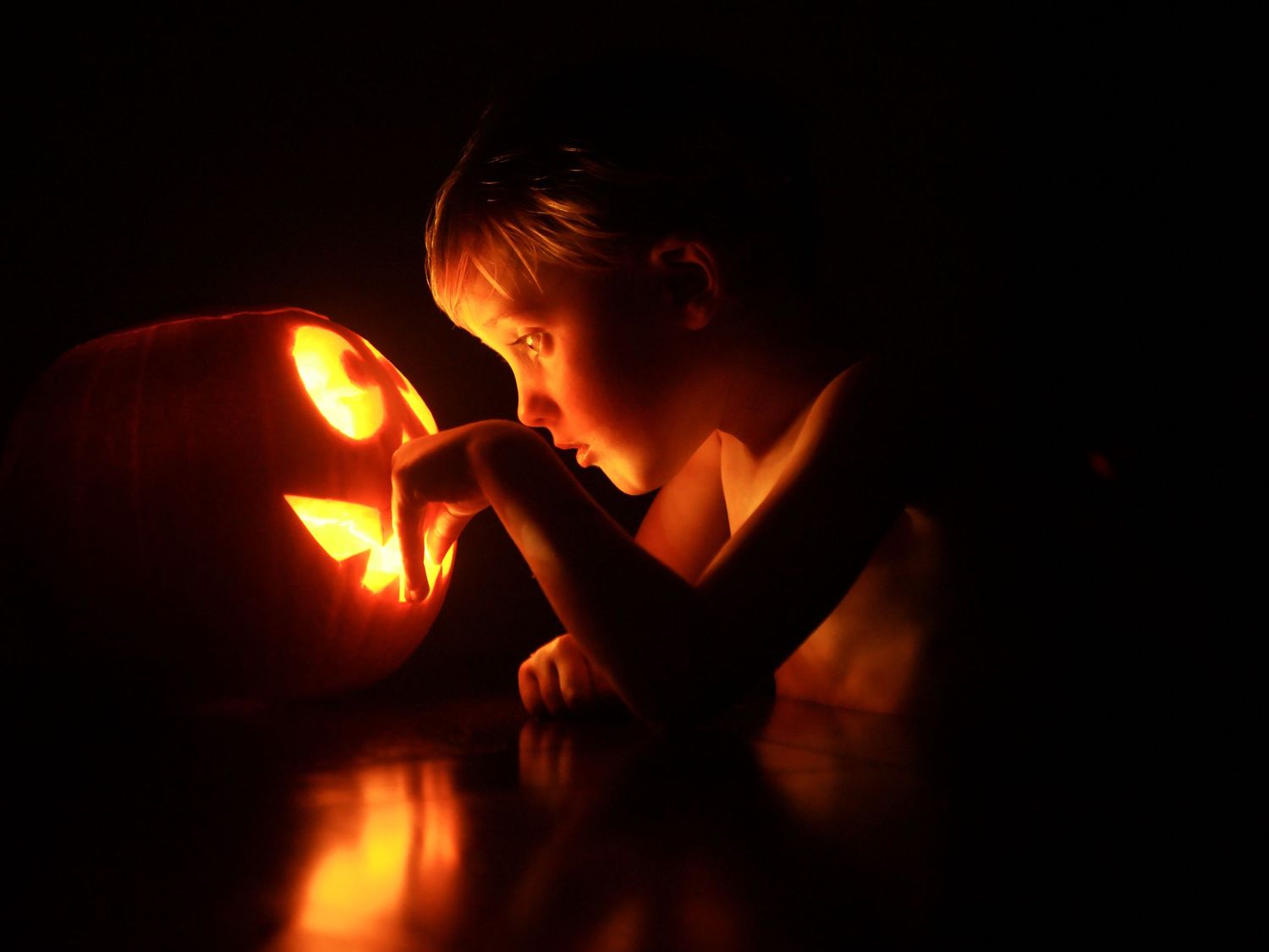 Silhouetted figure illuminated by warm candlelight creates a dramatic atmospheric scene in darkness.