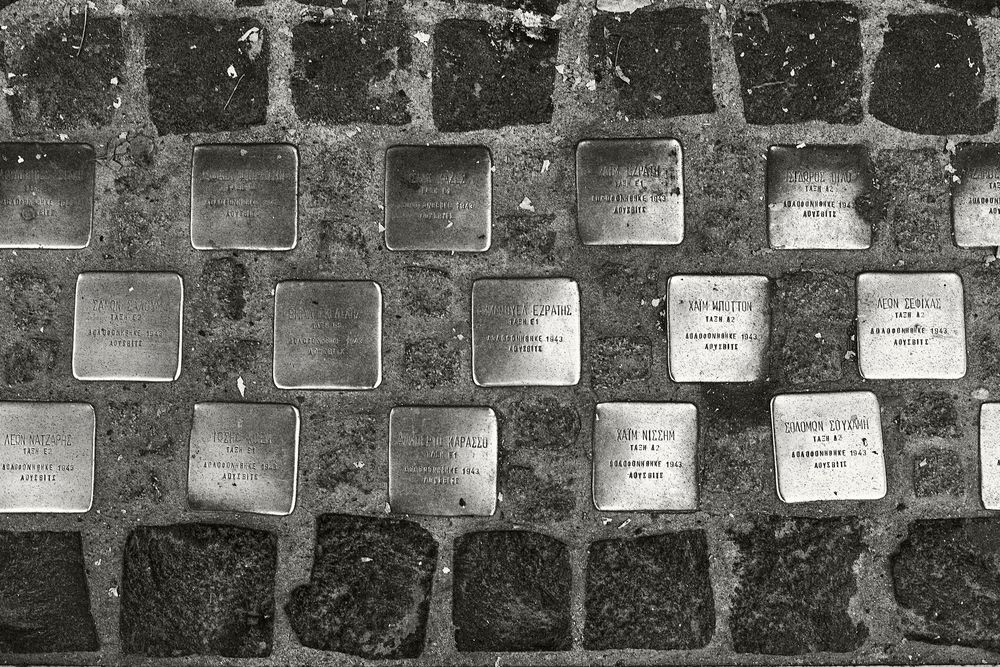 Memorial stones embedded in cobblestone pavement commemorate victims of Nazi persecution during World War II.