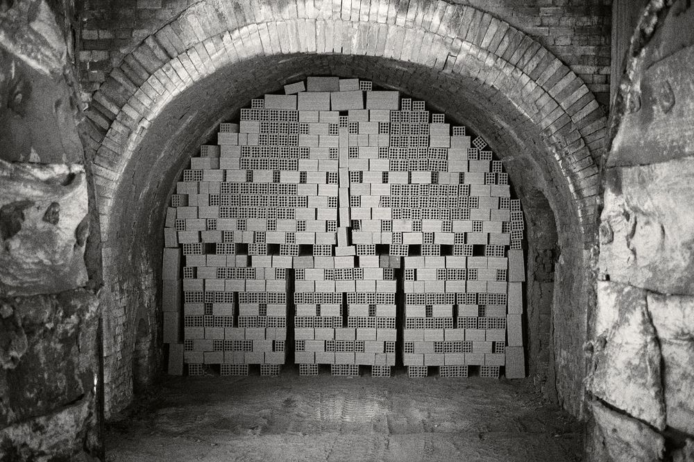 A series of brick tunnel archways with rough stone walls extend into darkness creating an atmospheric underground passage.