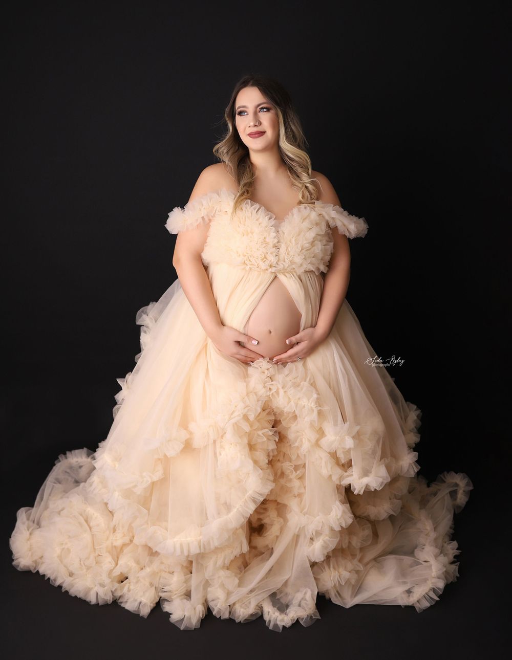 Ethereal peach-colored tulle maternity gown photographed against a dark background in a dramatic studio setting.
